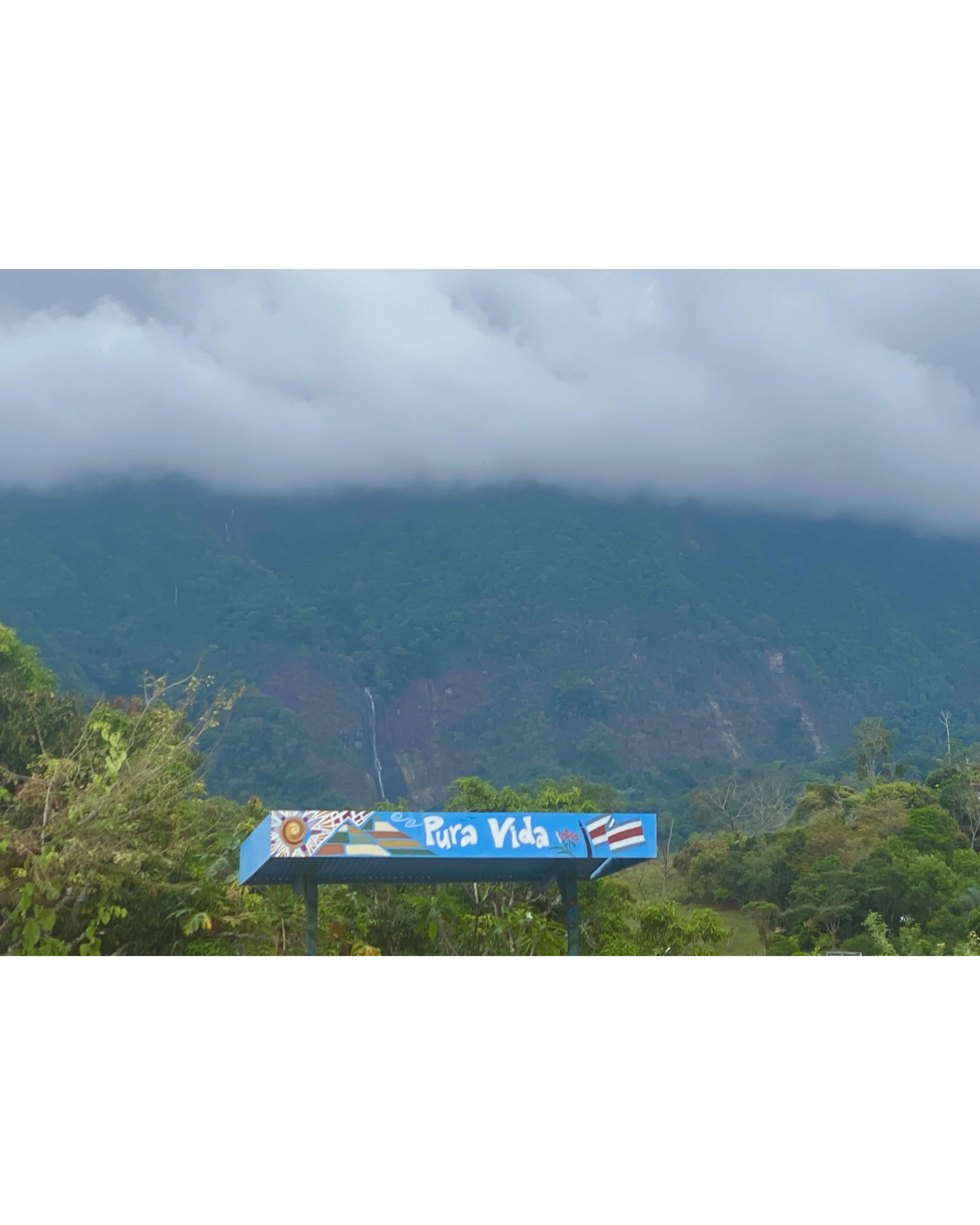 Pura Vida sign beneath cloud-covered mountains in Costa Rica